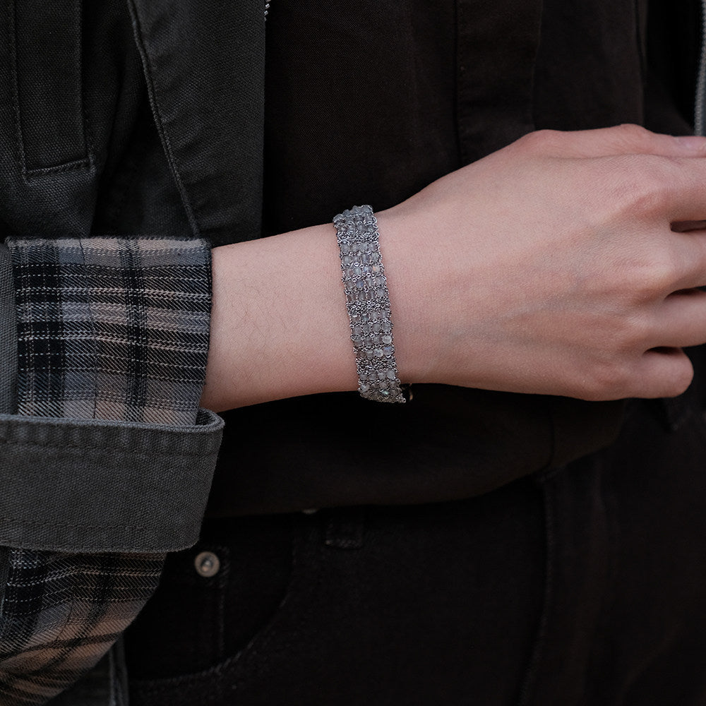 Between the Clouds handwoven crystal bracelet gold and silver variants with feather charms on moss, flat lay